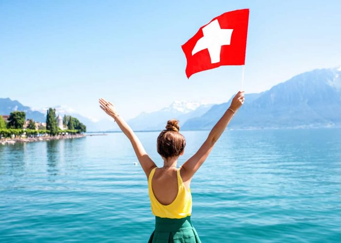 Woman holding Swiss flag in the air. Sicss National Day 2021.