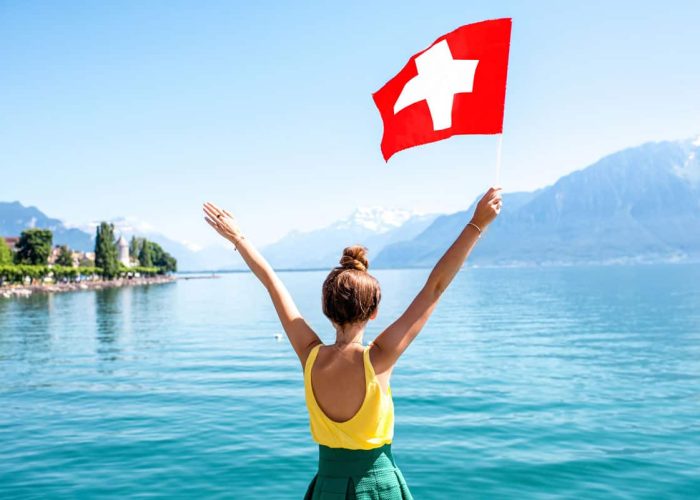 Woman holding Swiss flag in the air. Sicss National Day 2021.